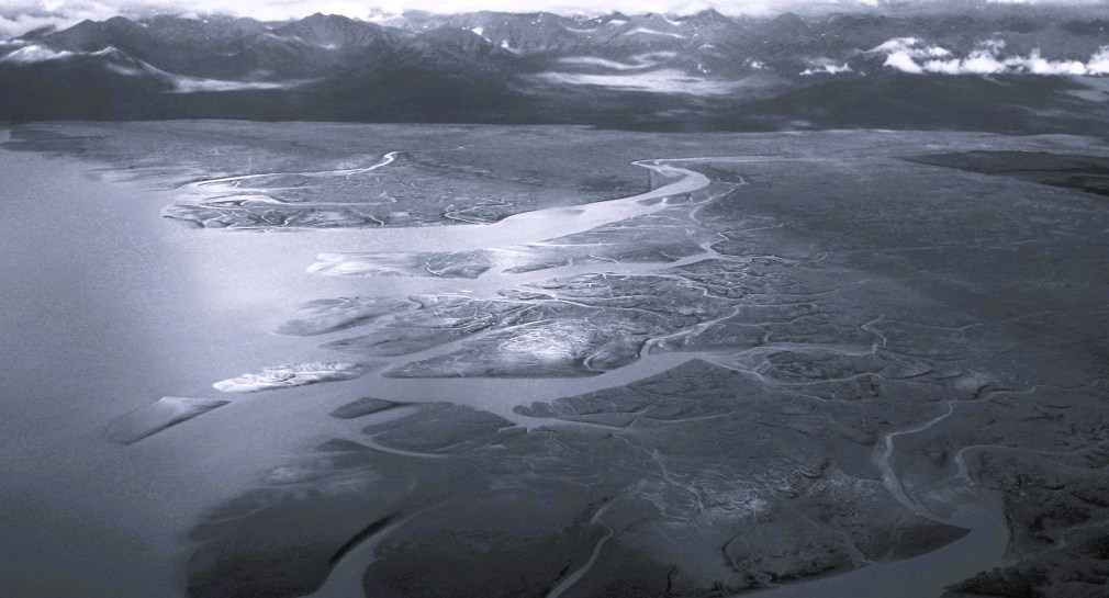 Black-and-white aerial view of a braided river branching across a delta toward distant mountains near the Bering Sea in Alaska