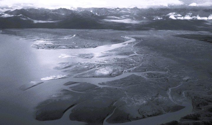 Black-and-white aerial view of a braided river branching across a delta toward distant mountains near the Bering Sea in Alaska